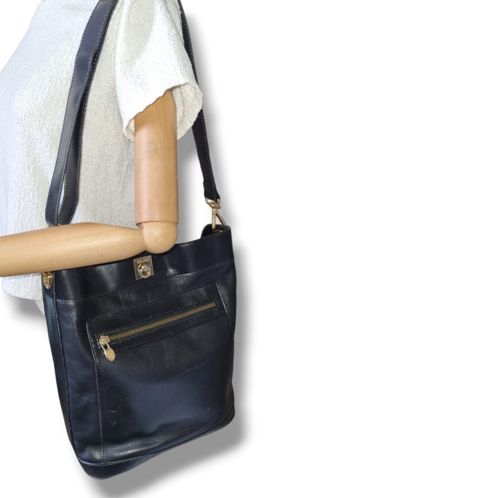 Sac Céline vintage noir en cuir lisse avec intérieur rouge et détails dorés porté épaule
